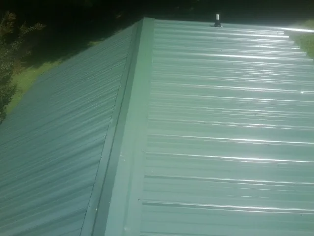 New green metal panels meeting at the ridge of a roof — Flat Roof Repair work by our crew in Palm Coast