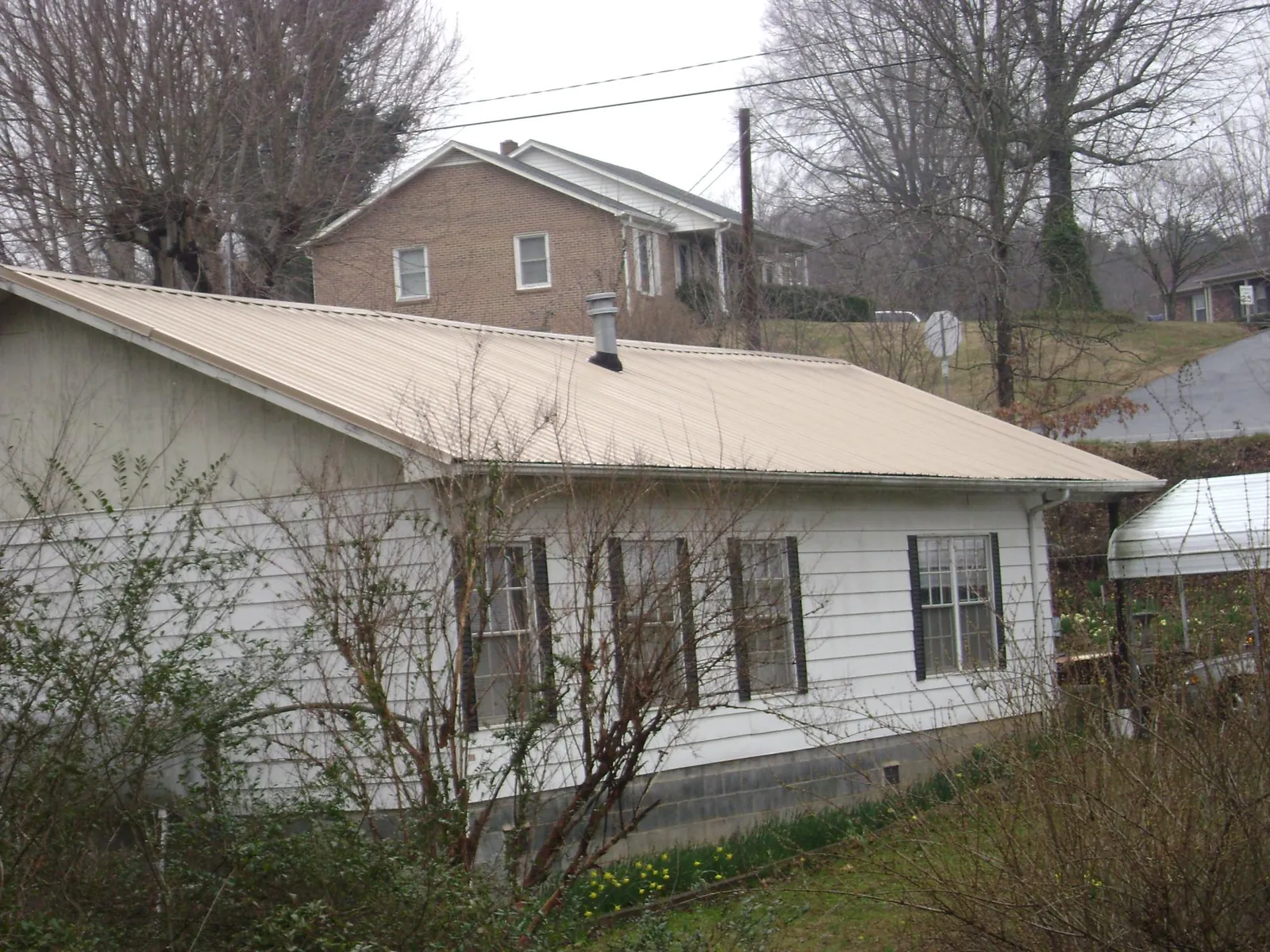 Tan metal roof on a white sided house set into a hillside — Commercial Roofing by Roofing Brothers in Palm Coast